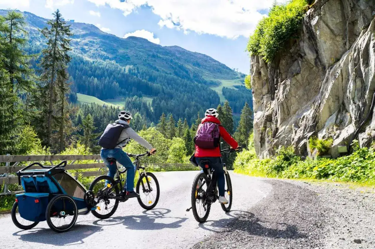 Zwei Radfahrer mit Rucksäcken und Anhänger fahren auf einer Bergstraße.
