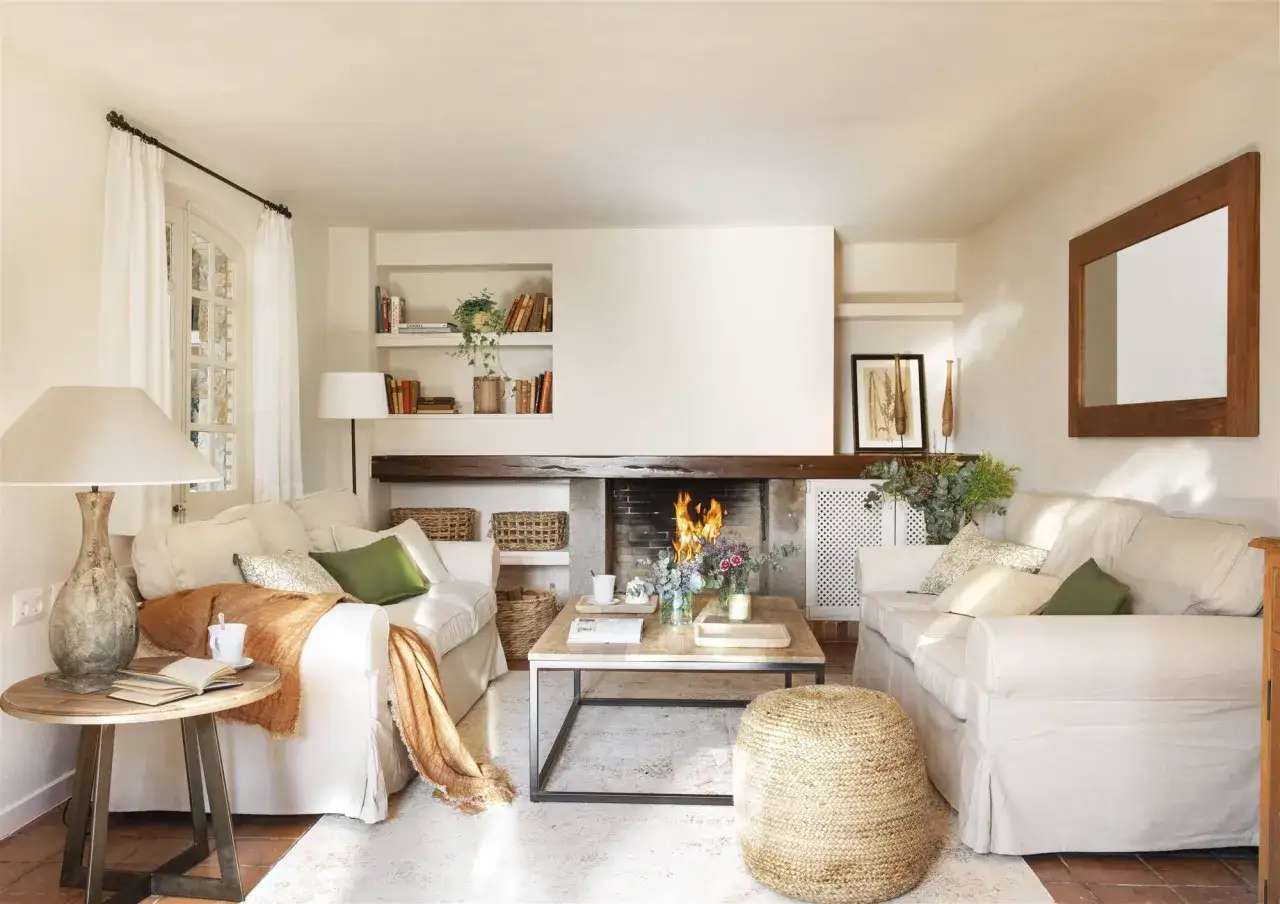 Salón acogedor con chimenea encendida, sofás blancos, mesa de centro de madera y detalles decorativos.