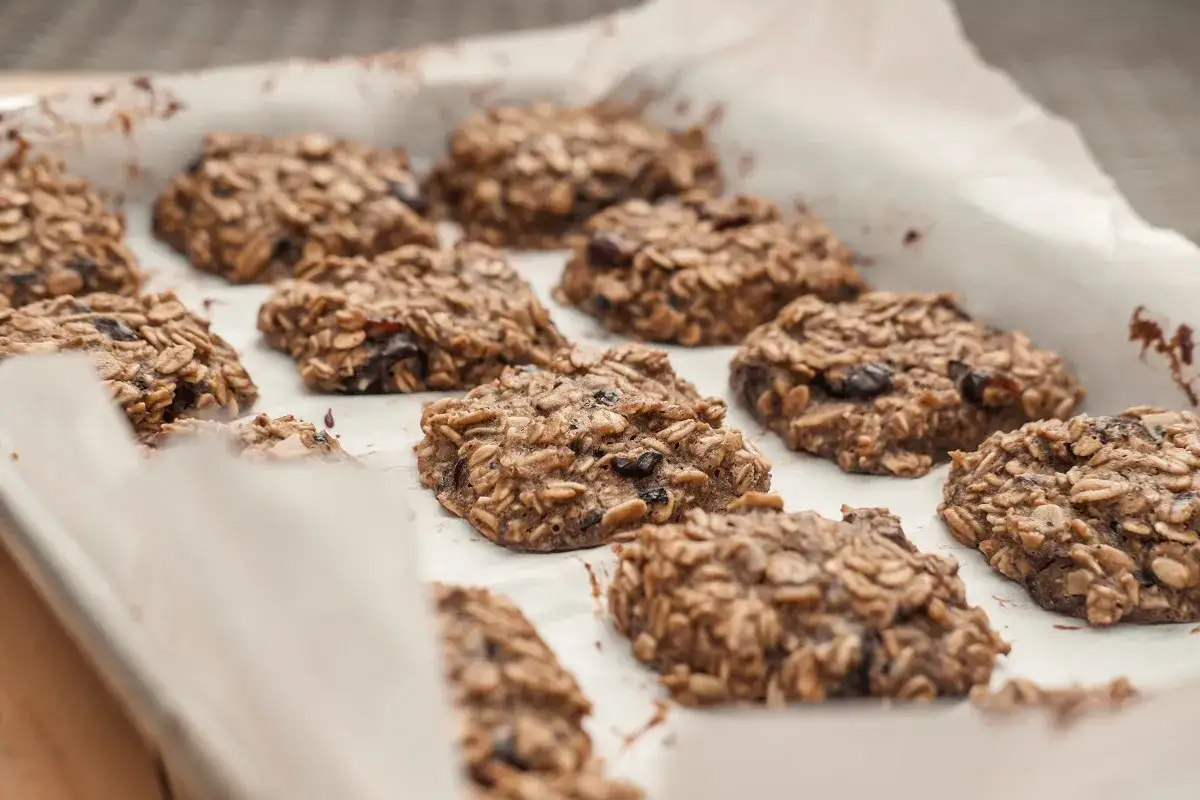 Na blasze wyłożonej papierem do pieczenia leżą świeżo upieczone, zdrowe ciasteczka owsiane z bakaliami. Idealne do kawy, jako przekąska lub element przepisu na zdrowe ciasteczka.