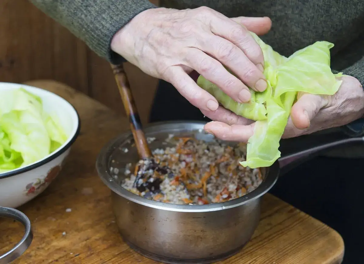 Ręce zwijają gołąbka, w garnku farsz z kaszą i warzywami. Zastanawiasz się, jakie przyprawy do farszu na gołąbki?