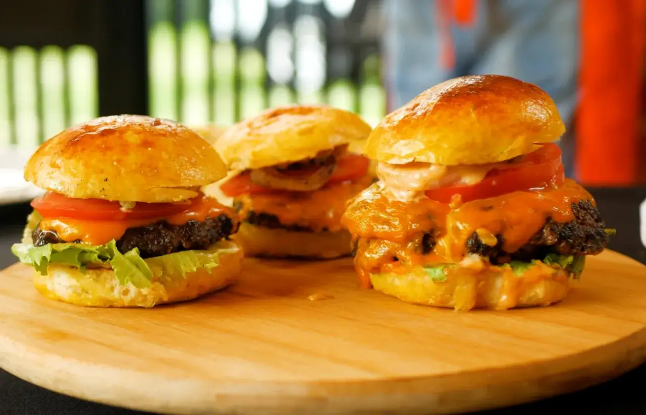 Trzy soczyste burgery z roztopionym serem, pomidorem i sałatą na desce.