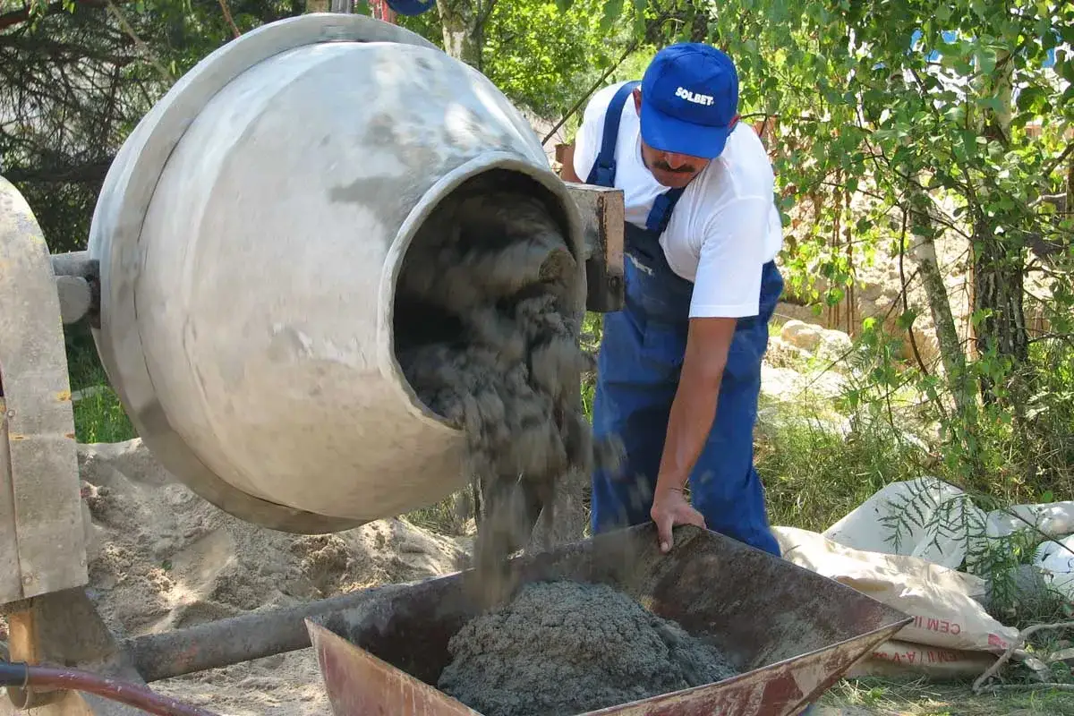 Robot budowlany wylewa zaprawę tynkarską z betoniarki do taczki.