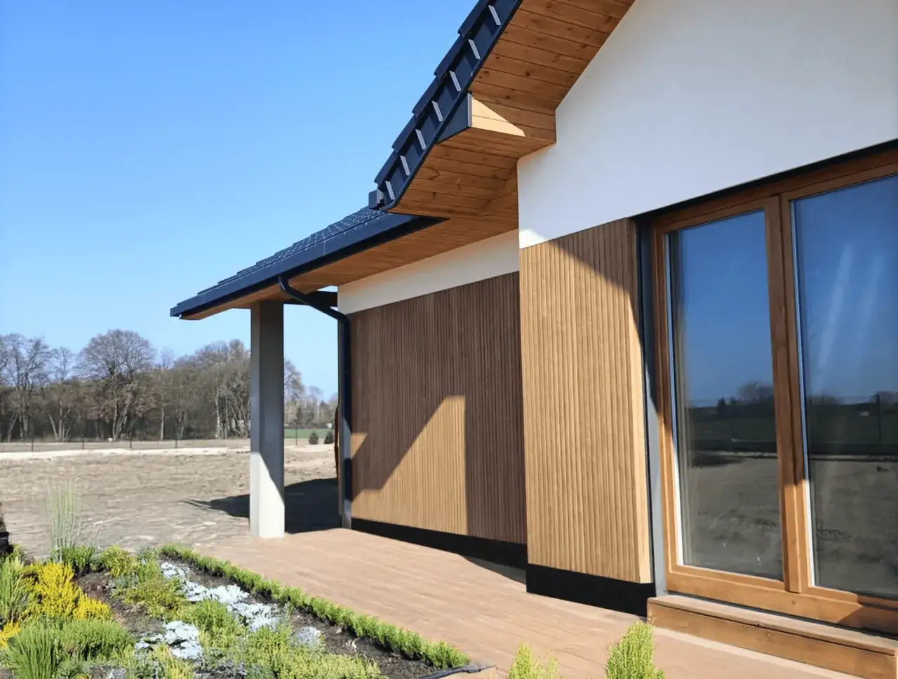 Fragment nowoczesnego domu z drewnianą elewacją lamelową i dużym oknem.