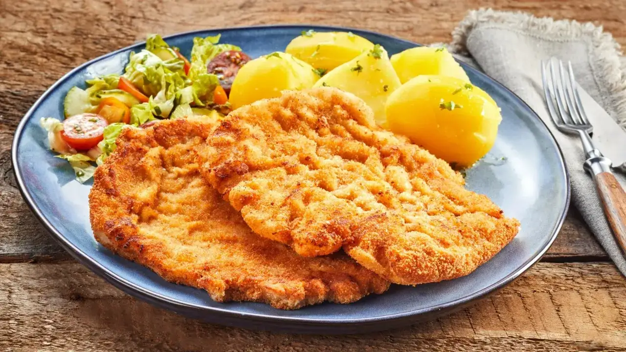 Dwa chrupiące kotlety, jeden sznycel cielęcy, drugi kotlet schabowy, podane z ziemniakami i sałatką.