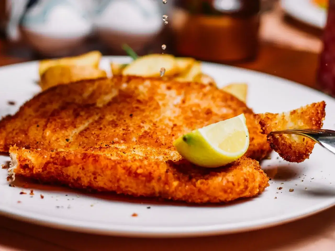 Chrupiący panierowany filet rybny z frytkami i ćwiartką cytryny na białym talerzu.