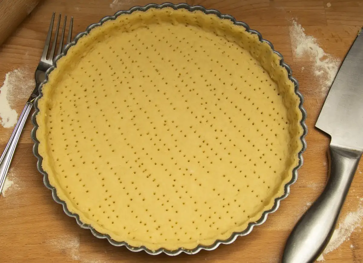 Gotowy spód do tarty, przygotowany według przepisu na ciasto kruche z olejem. Widoczne narzędzia: widelec i nóż.
