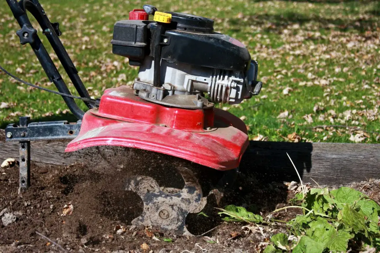 Czerwona glebogryzarka z czarnym silnikiem pracuje w ziemi, rozbijając ją.