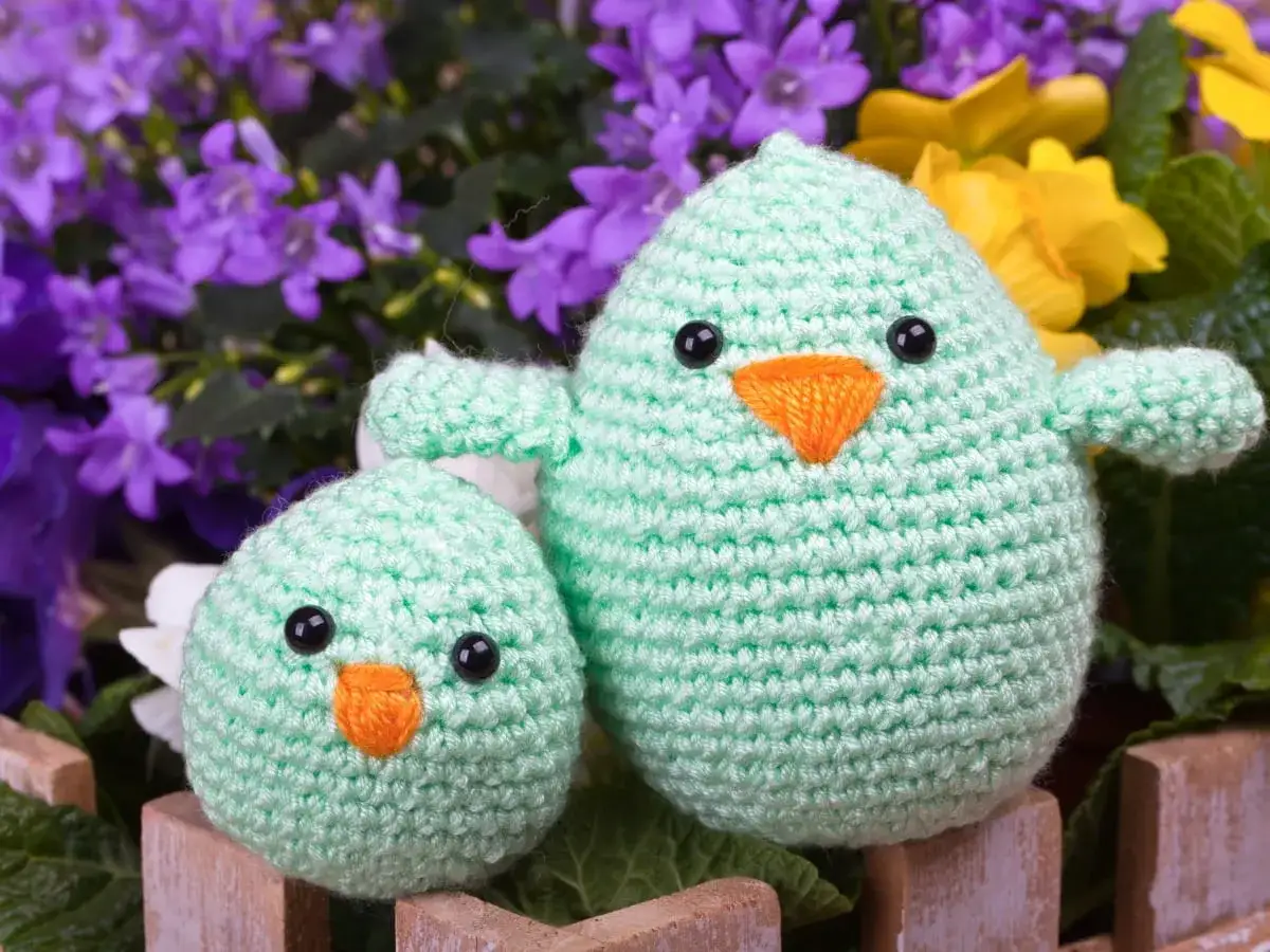 Urocze, miętowe kurczaczki z szydełku, siedzące wśród wiosennych kwiatów. Idealne dekoracje wielkanocne.