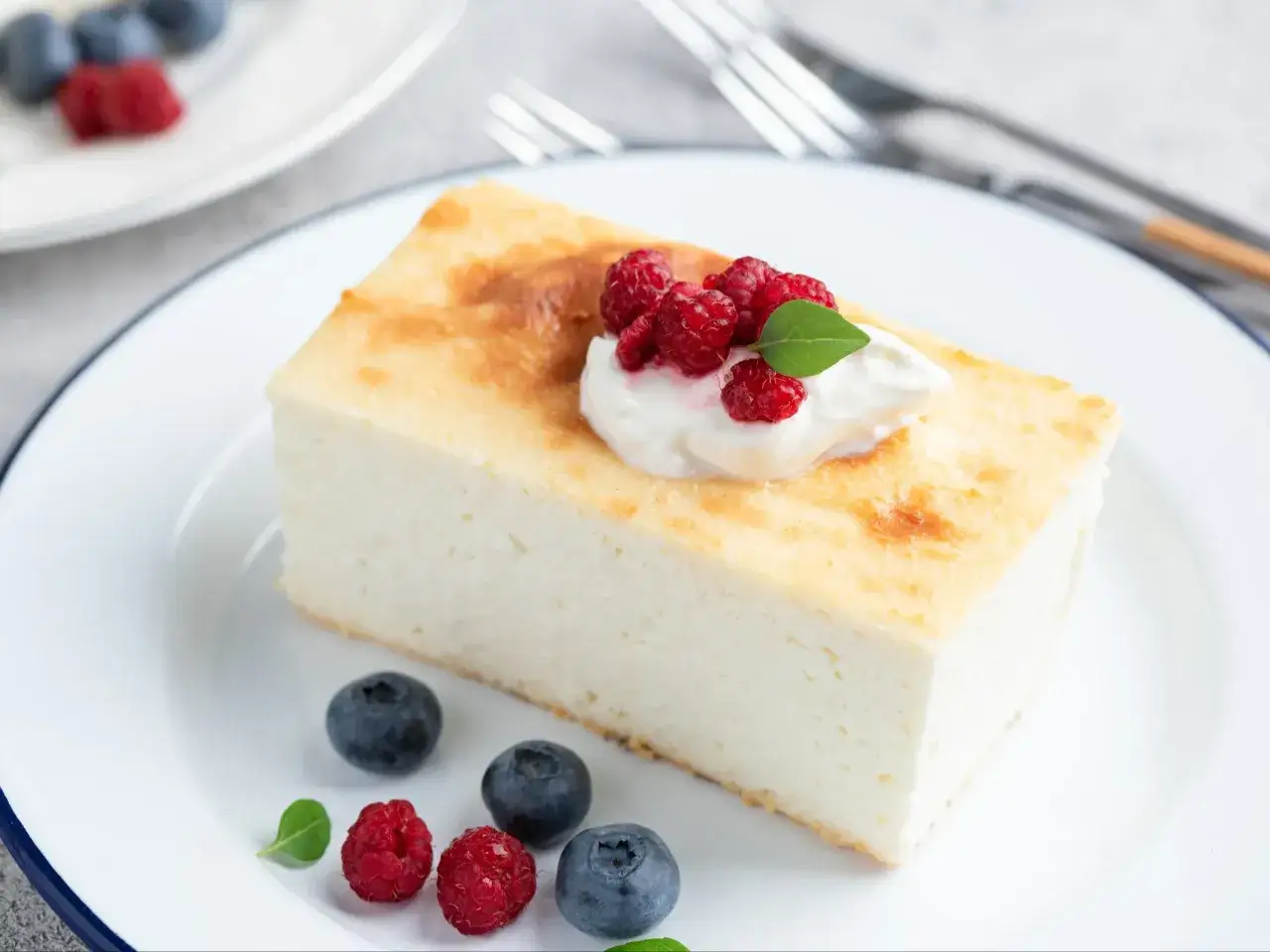 Puszysty sernik, który nie opada, udekorowany bitą śmietaną, malinami i borówkami. Idealny przepis na udane wypieki.