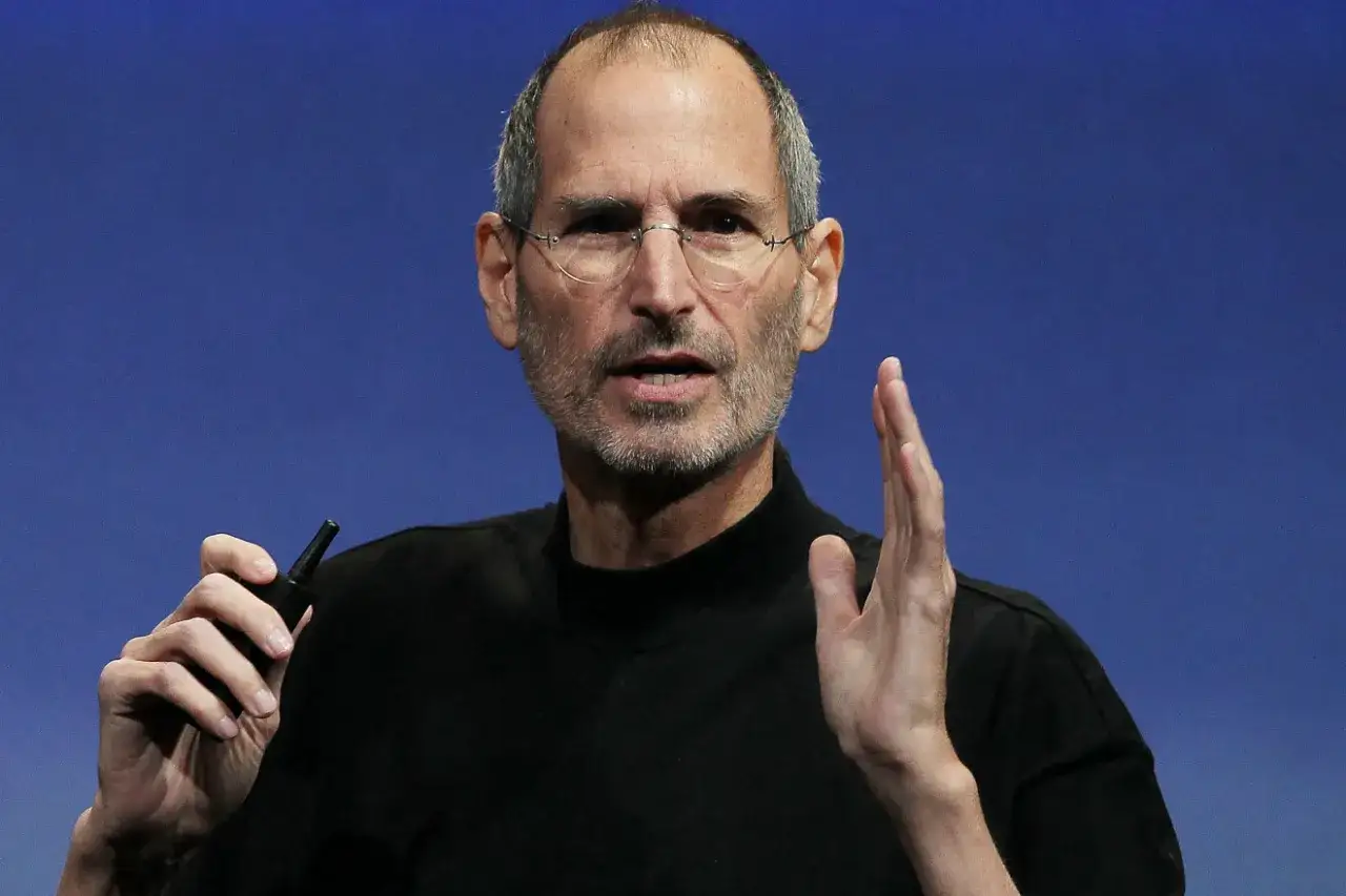 Steve Jobs, w okularach i czarnym golfie, trzyma w dłoni mały przedmiot. Ciekawe fakty o jego życiu i karierze.