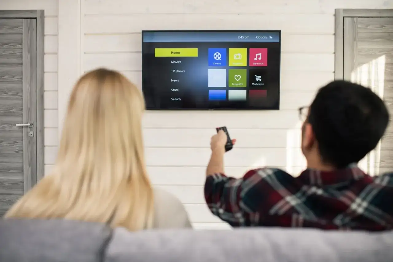 Para relaksuje się przy muzyce. Na ekranie telewizora widać menu aplikacji, w tym "My music", które przypomina interfejs Spotify na telewizorze.