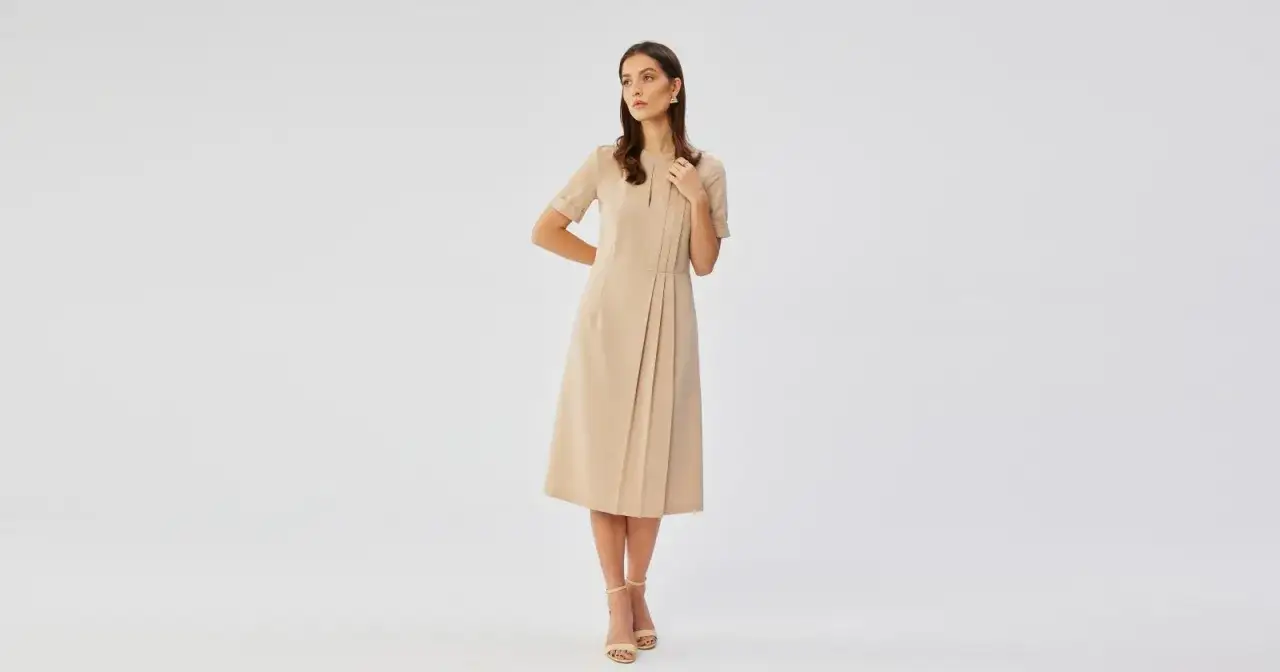 Elegancka beżowa sukienka to idealna propozycja, jak się ubrać na wesele po 50. Klasyczna, ale stylowa.