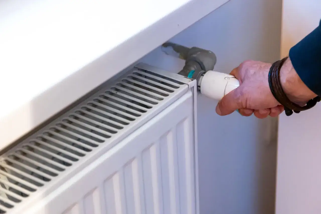 Ręka reguluje termostat grzejnika. Dowiedz się, jak wymienić kaloryfer w bloku, by cieszyć się ciepłem.