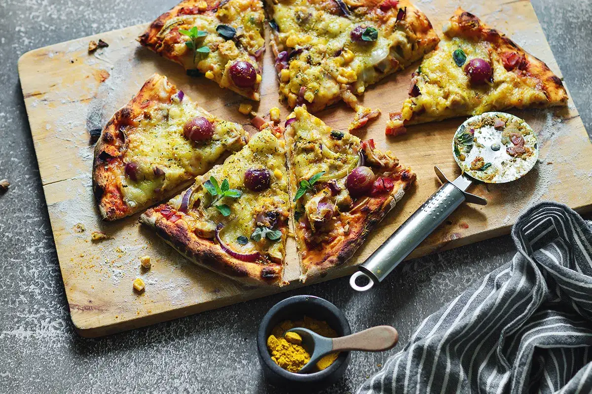 Domowa pizza z kurczakiem, kukurydzą i czerwoną cebulą, pokrojona na kawałki, gotowa do podania.