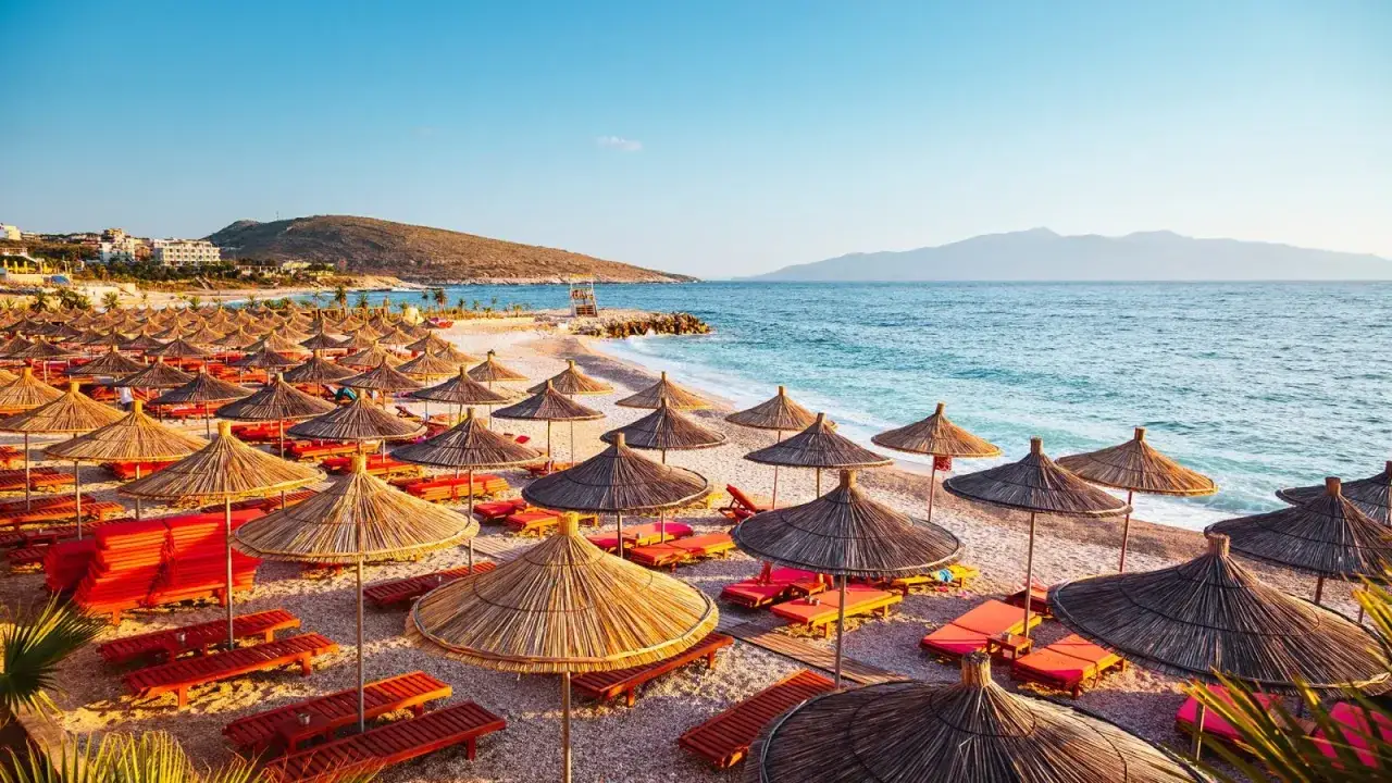 Albania, lipiec: słoneczna plaża z rzędami parasoli i leżaków, turkusowe morze i góry w tle. Idealna pogoda na wakacje.