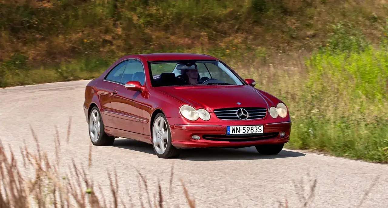 Czerwony Mercedes CLK W209 z kierowcą przemierza malowniczą, wiejską drogę.
