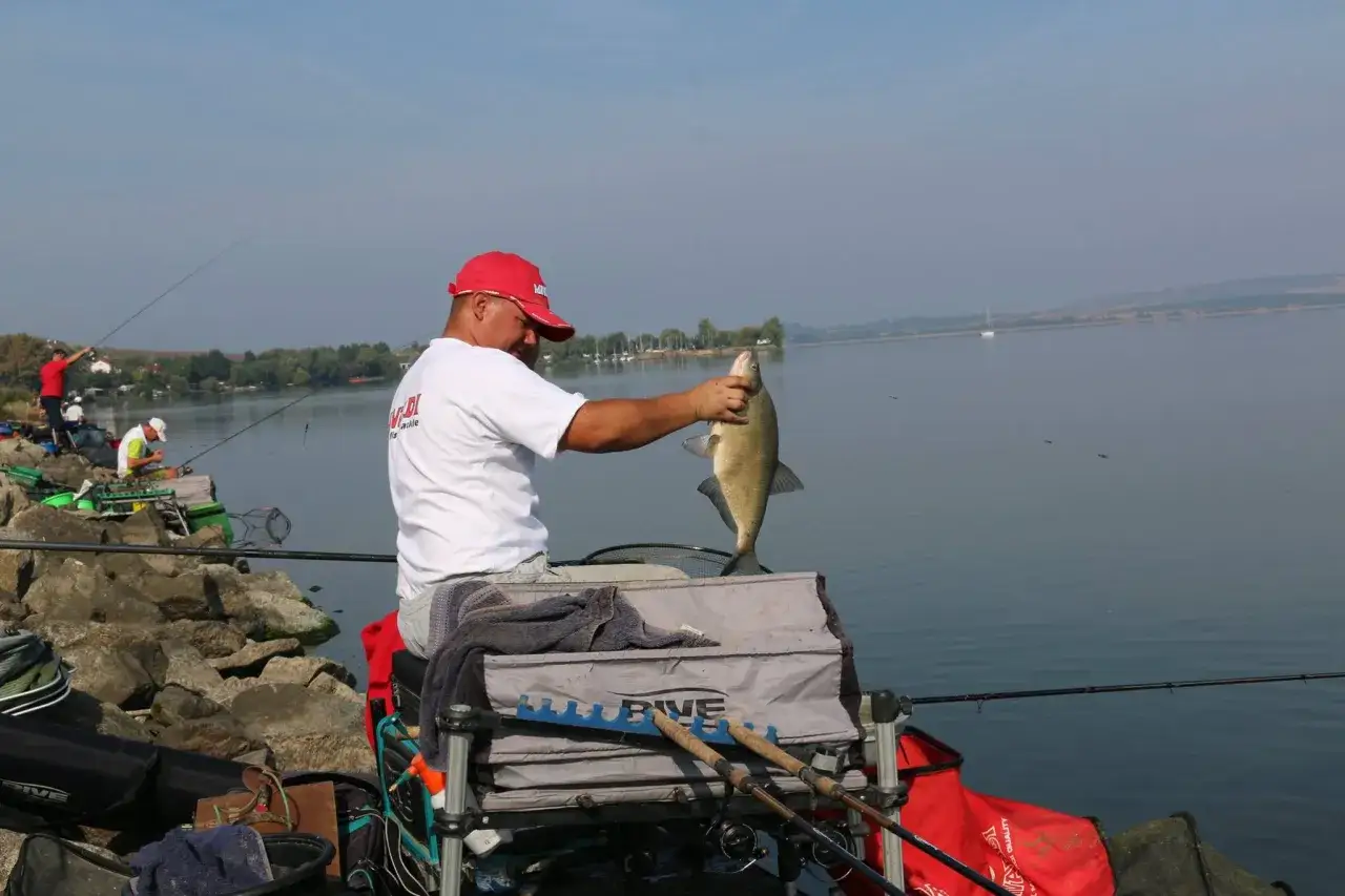 Wędkarz z dumą prezentuje złowioną rybę, obok stoi pojemnik z zanętą Champion Feed.