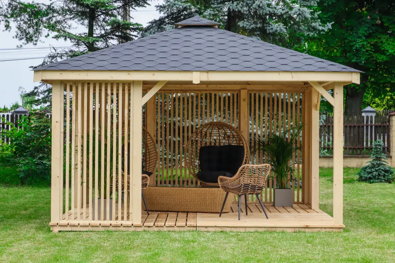 Drewniana altana 3x3 z meblami i roślinami. Dach pokryty ciemnym gontem. Idealna na relaks.