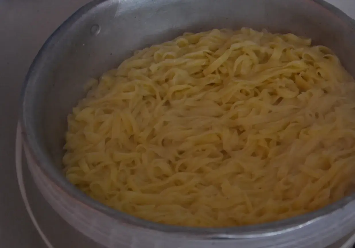 Gotowanie kluski vs makaron. Szerokie, żółte wstążki w garnku, gotowe do podania.