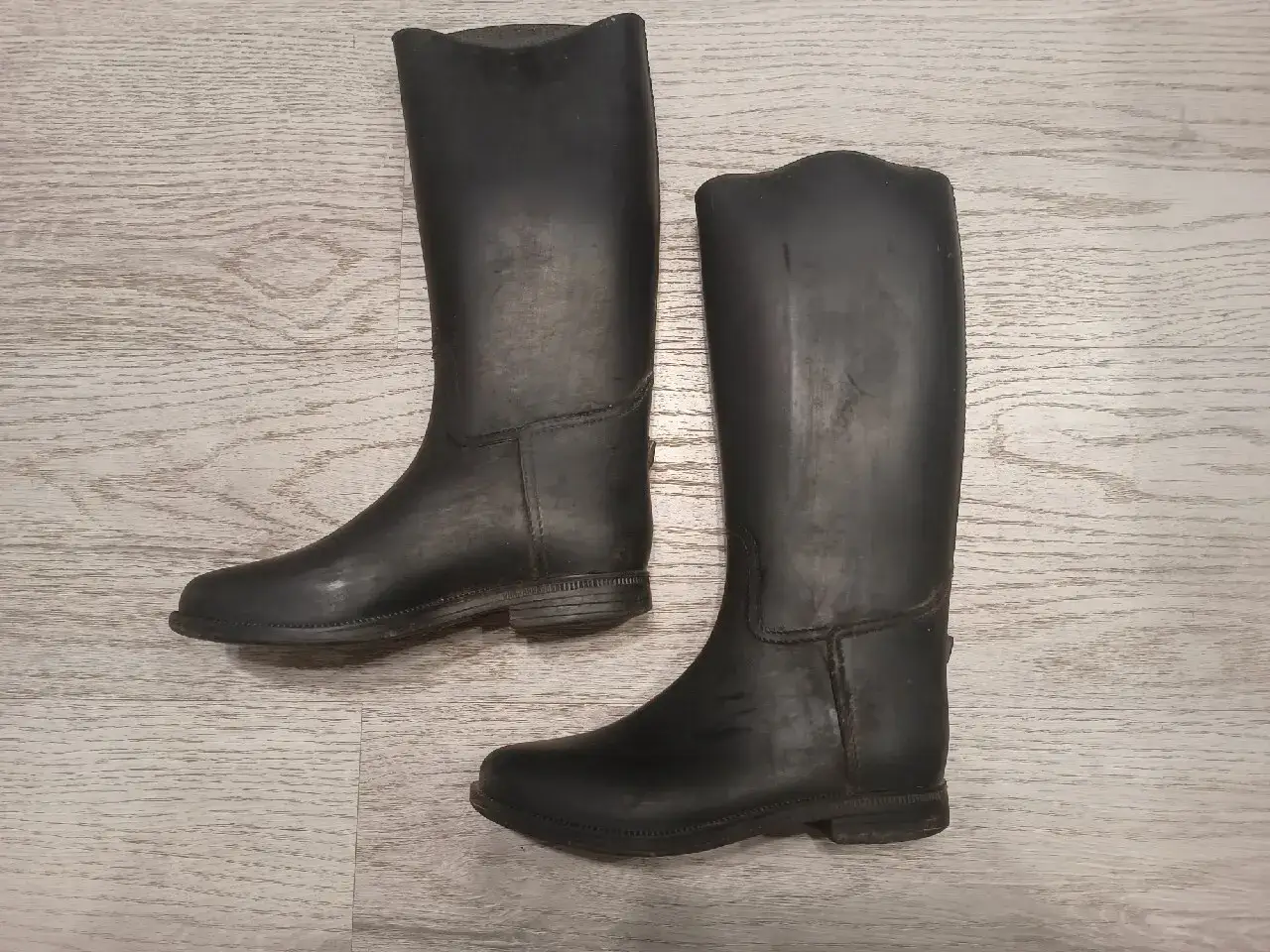 Para czarnych gumowych kaloszy jeździeckich na jasnym, drewnianym tle.