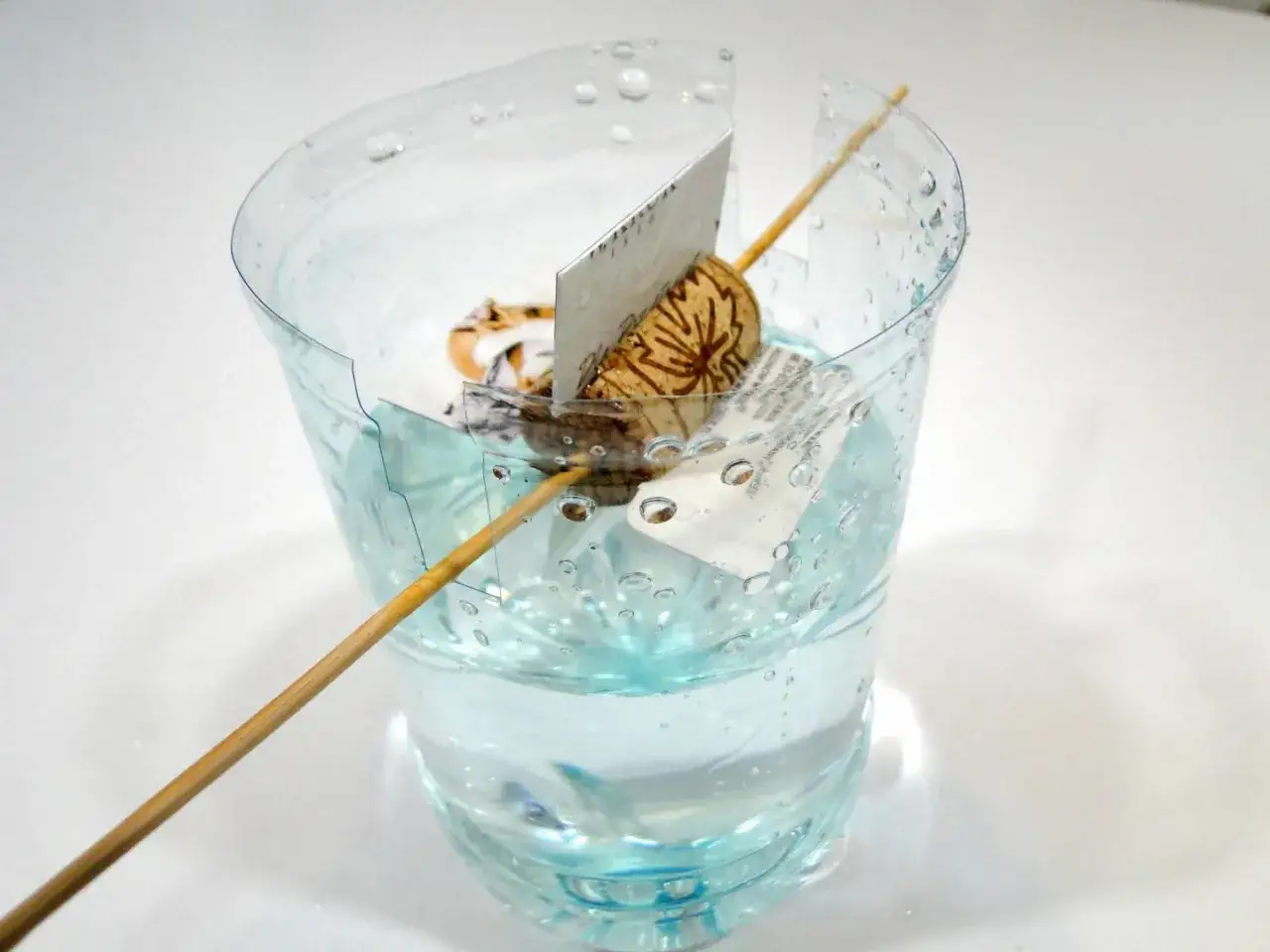 Miniaturowa turbina wodna z patyczka i orzecha w szklance z wodą.