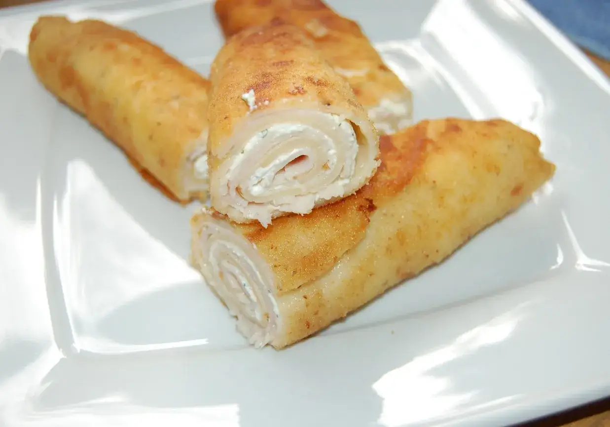 Złociste naleśniki z szynką i serem, zawinięte w apetyczne ruloniki, kuszą swoim wyglądem.