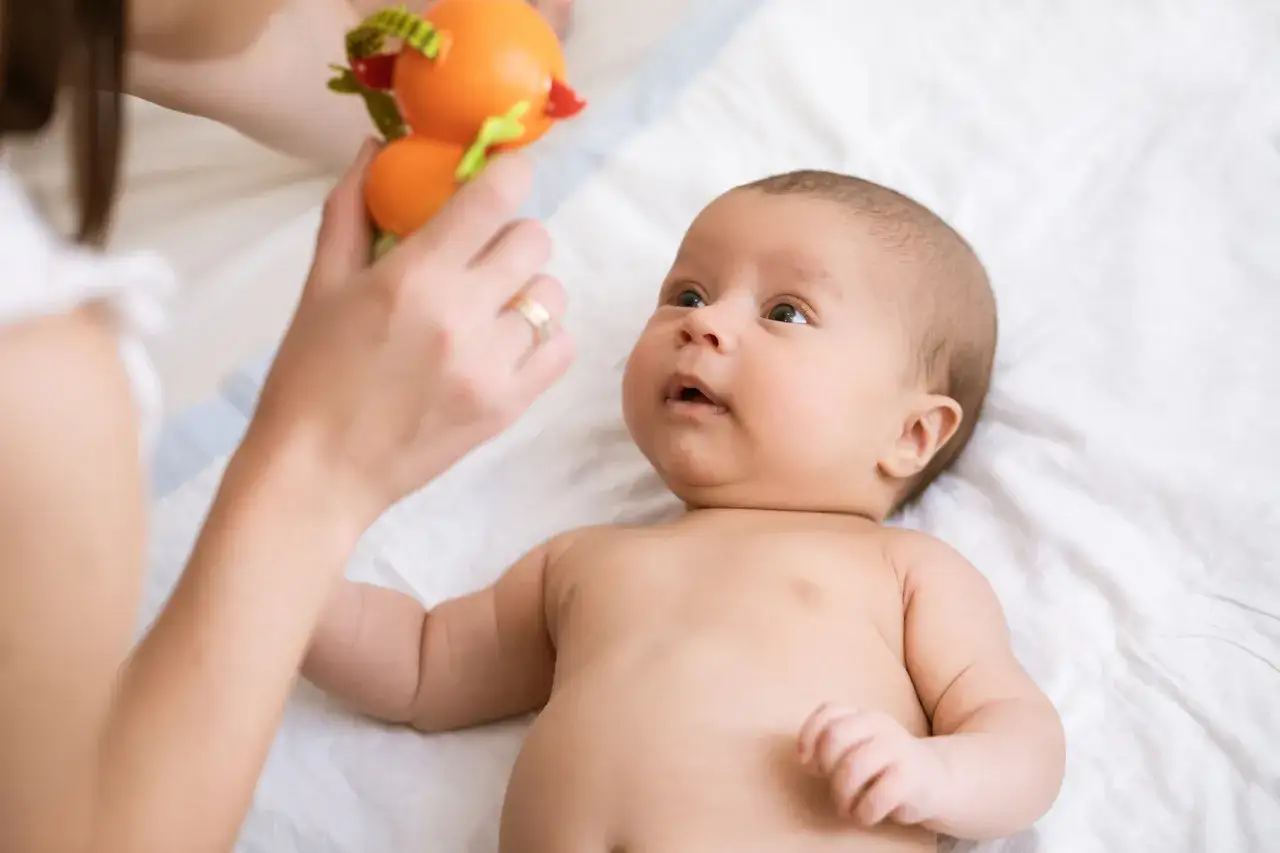 Co widzi tygodniowe dziecko? Zaciekawiony noworodek patrzy na kolorową zabawkę trzymaną przez mamę.