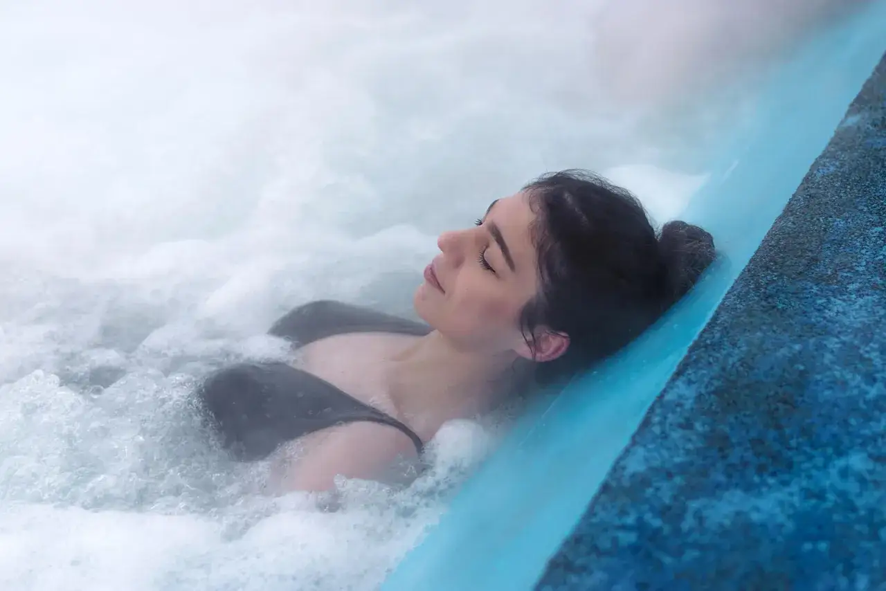 Kobieta relaksuje się w gorącej wodzie. Pomyśl, co zabrać ze sobą na termy: ręcznik, klapki i strój kąpielowy.