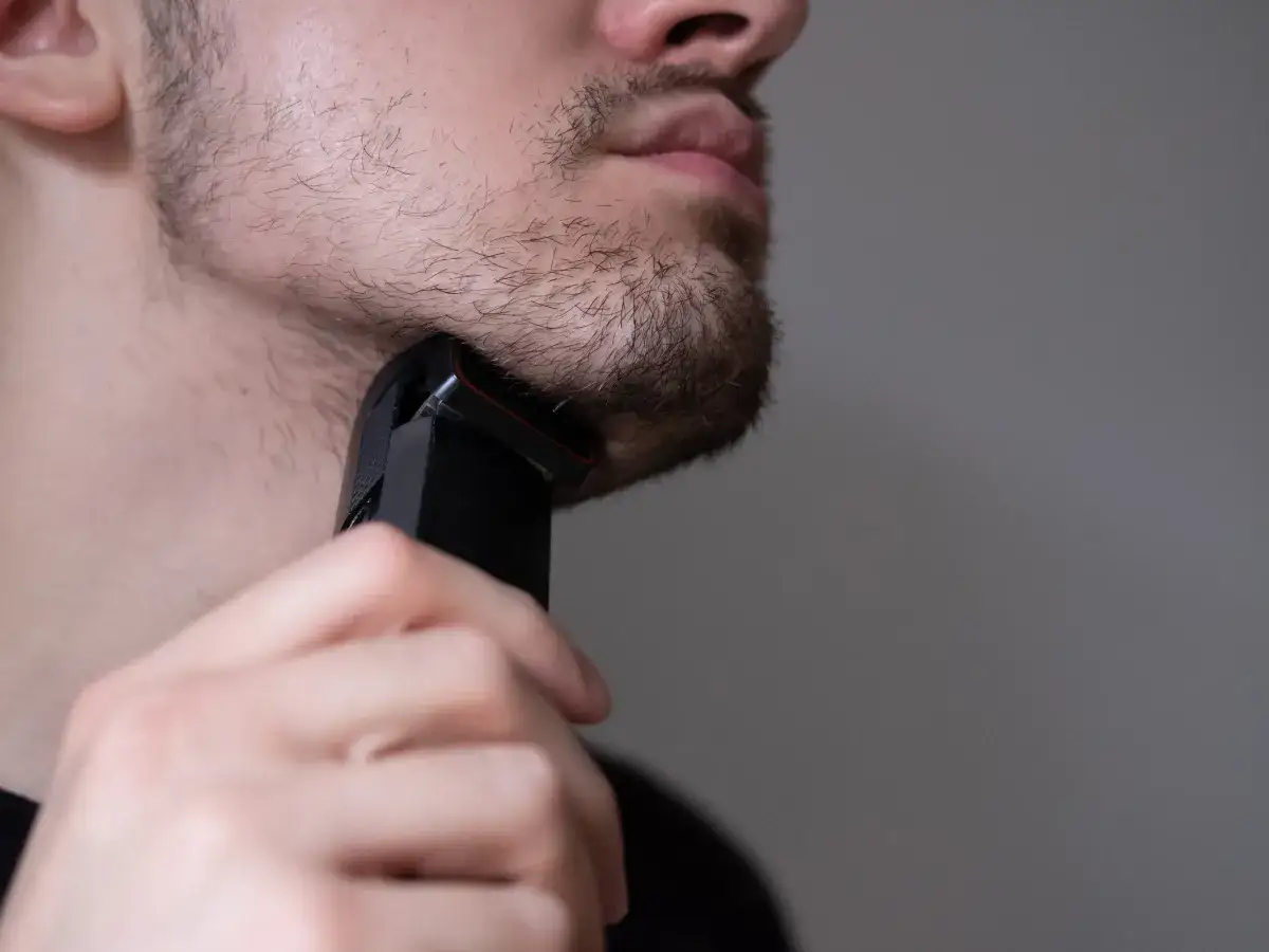 Mężczyzna goli zarost na brodzie czarną golarką.