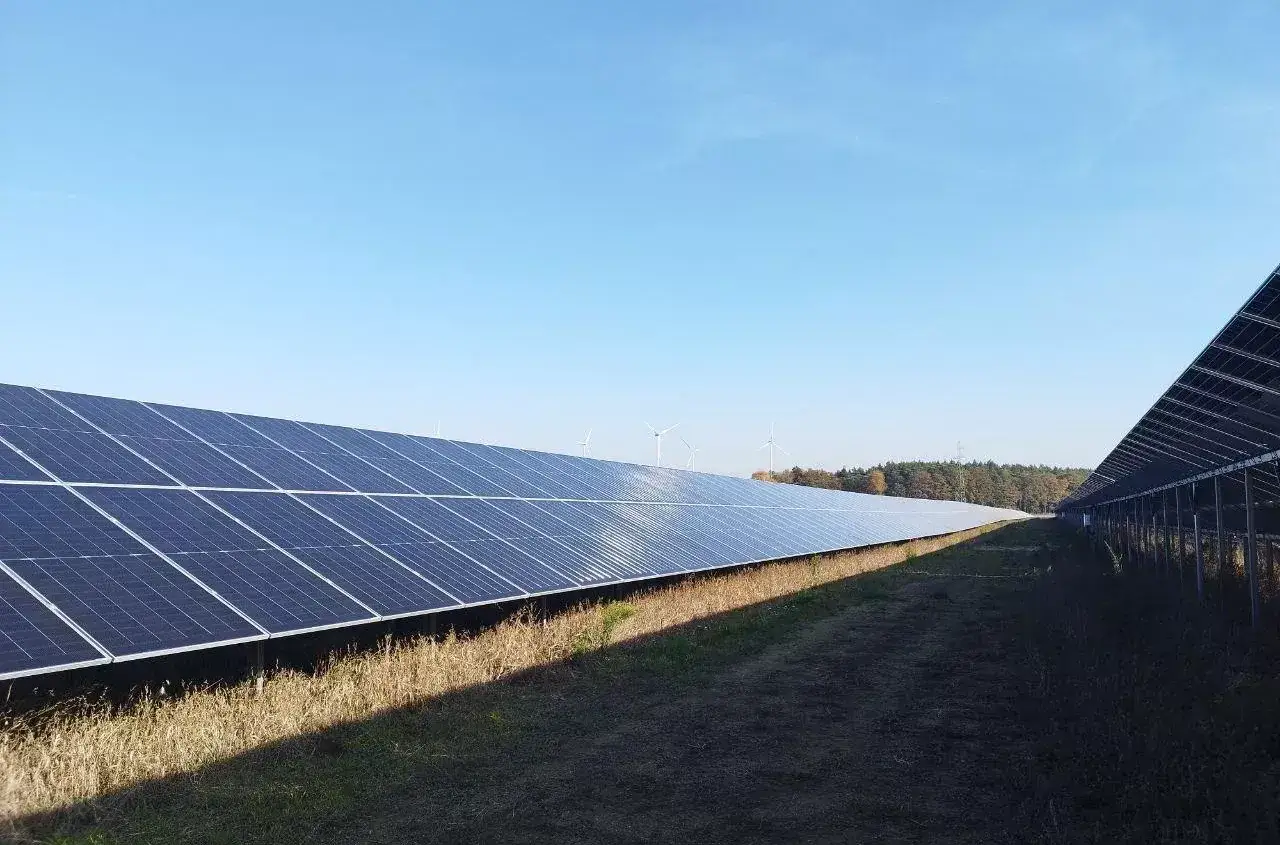 Panele fotowoltaiczne i wiatraki na tle błękitnego nieba. Kto płaci podatek od nieruchomości przy umowie dzierżawy?