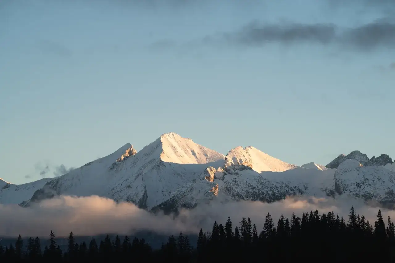 Złote słońce oświetla ośnieżone szczyty Tatr. W dole ciemny las, a nad nim mgła. Idealne miejsce na narty, jak w Bukowinie Tatrzańskiej wyciągi.