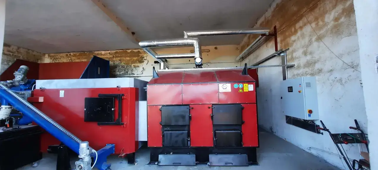 W domu działa mała kotłownia z dwoma dużymi, czerwonymi kotłami i niebieskim podajnikiem paliwa.