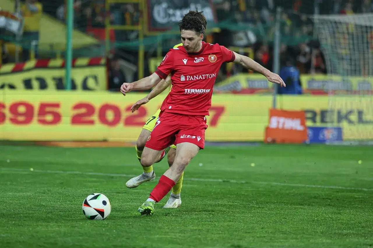 GKS Katowice piłkarze w akcji. Zawodnik w czerwonej koszulce drybluje z piłką na boisku, walcząc o zwycięstwo.