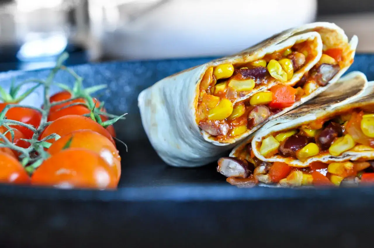 Pyszne burrito z kukurydzą, fasolą i papryką. Czy tortilla jest wegańska? Wygląda na to, że tak! Obok świeże pomidorki.
