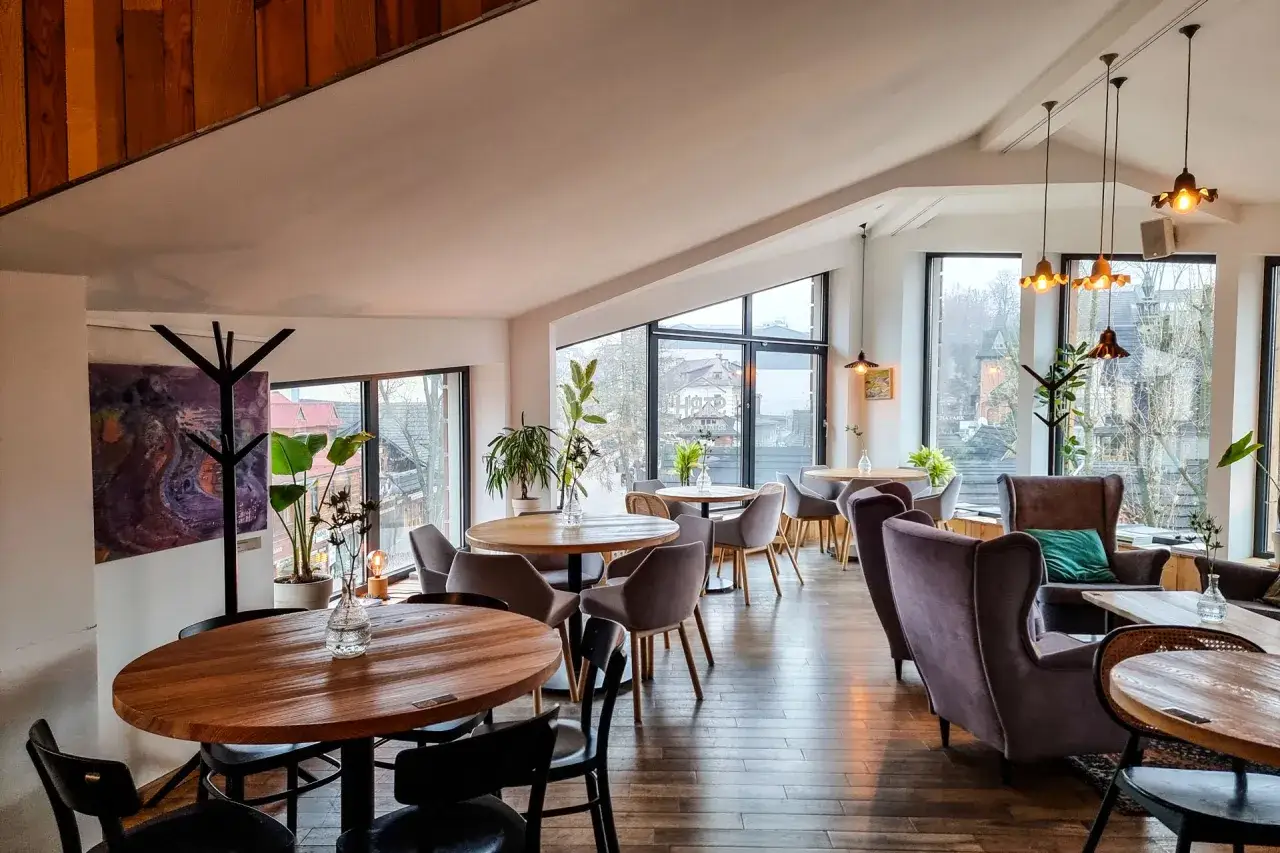 Przytulna restauracja w Bukowinie Tatrzańskiej z widokiem na góry. Drewniane stoły, wygodne fotele i stylowe oświetlenie tworzą ciepłą atmosferę.
