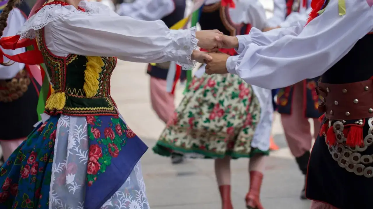 Tancerze w barwnych strojach ludowych, żywa muzyka folkowa w tle.
