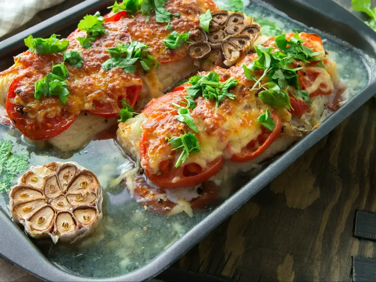 Pieczony dorsz z pomidorami i serem, podany z pieczoną główką czosnku. Idealny sposób, jak przyrządzić dorsza dietetycznie.