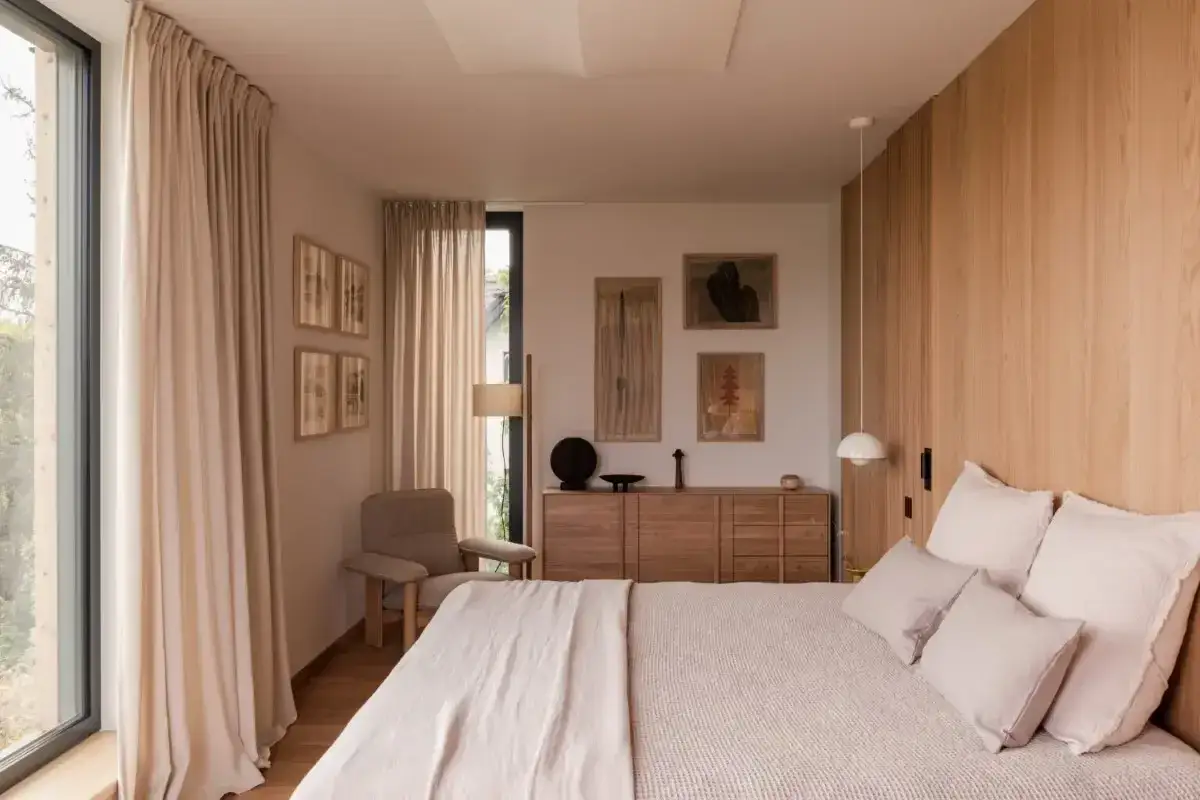 Przytulna sypialnia z łóżkiem, drewnianą komodą, fotelem i obrazami na ścianie.