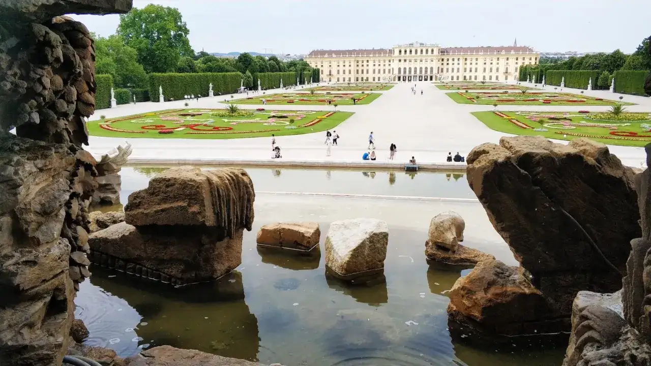 Wiedeń ogrody Sisi: malowniczy widok na pałac Schönbrunn i jego kwieciste tarasy, z kamienną fontanną w pierwszym planie.