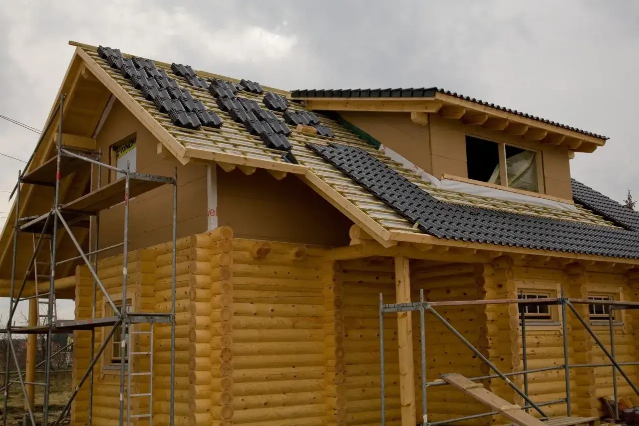 Budowa domu z bali, trwa układanie dachówki. Trudno oszacować ile m3 drewna na dom z bali, ale konstrukcja wygląda solidnie.