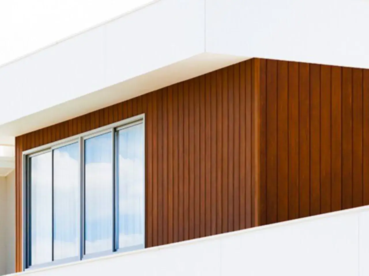 Nowoczesny budynek z białymi elementami i brązowymi, pionowymi lamelami zewnętrznymi. Duże okna odbijają błękitne niebo.