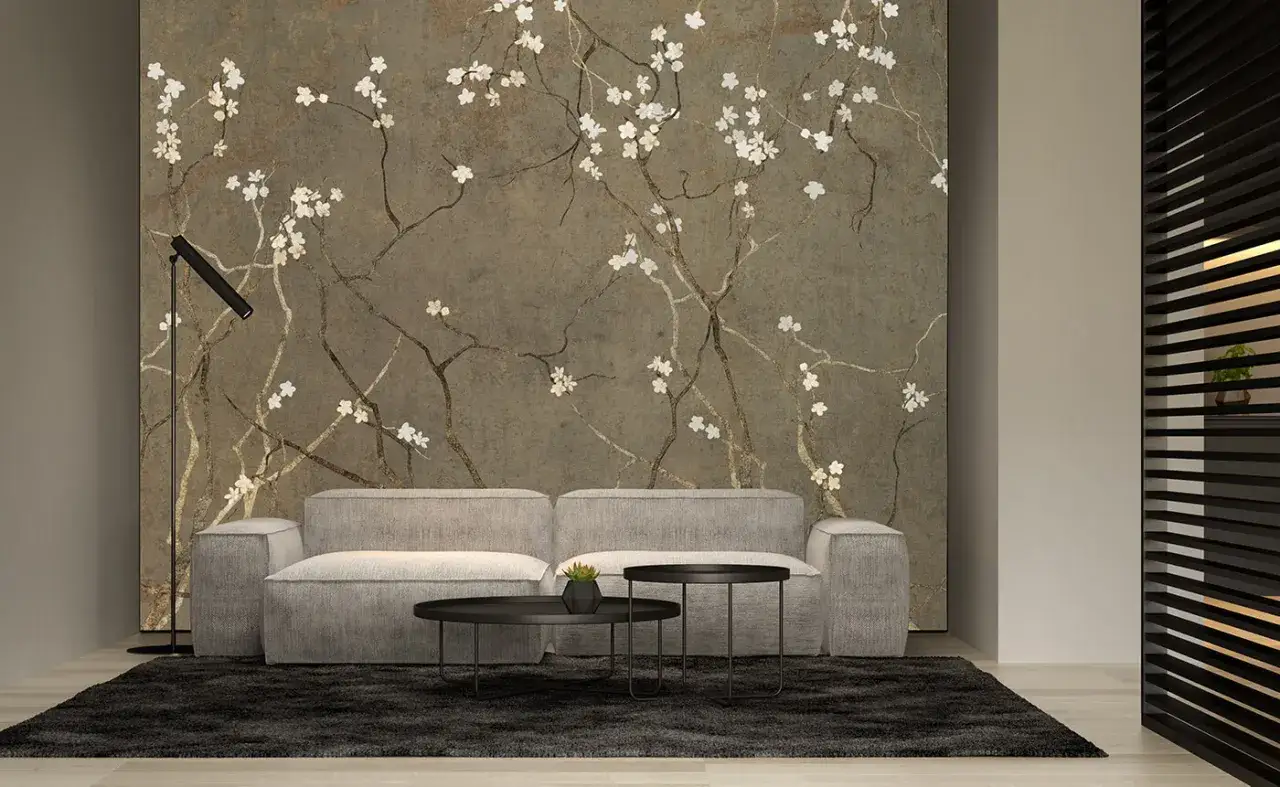 Eleganckie tapety z drzewami kwitnącymi na tle kamiennej ściany. Jasnoszara kanapa i czarne stoliki dopełniają nowoczesny wystrój.