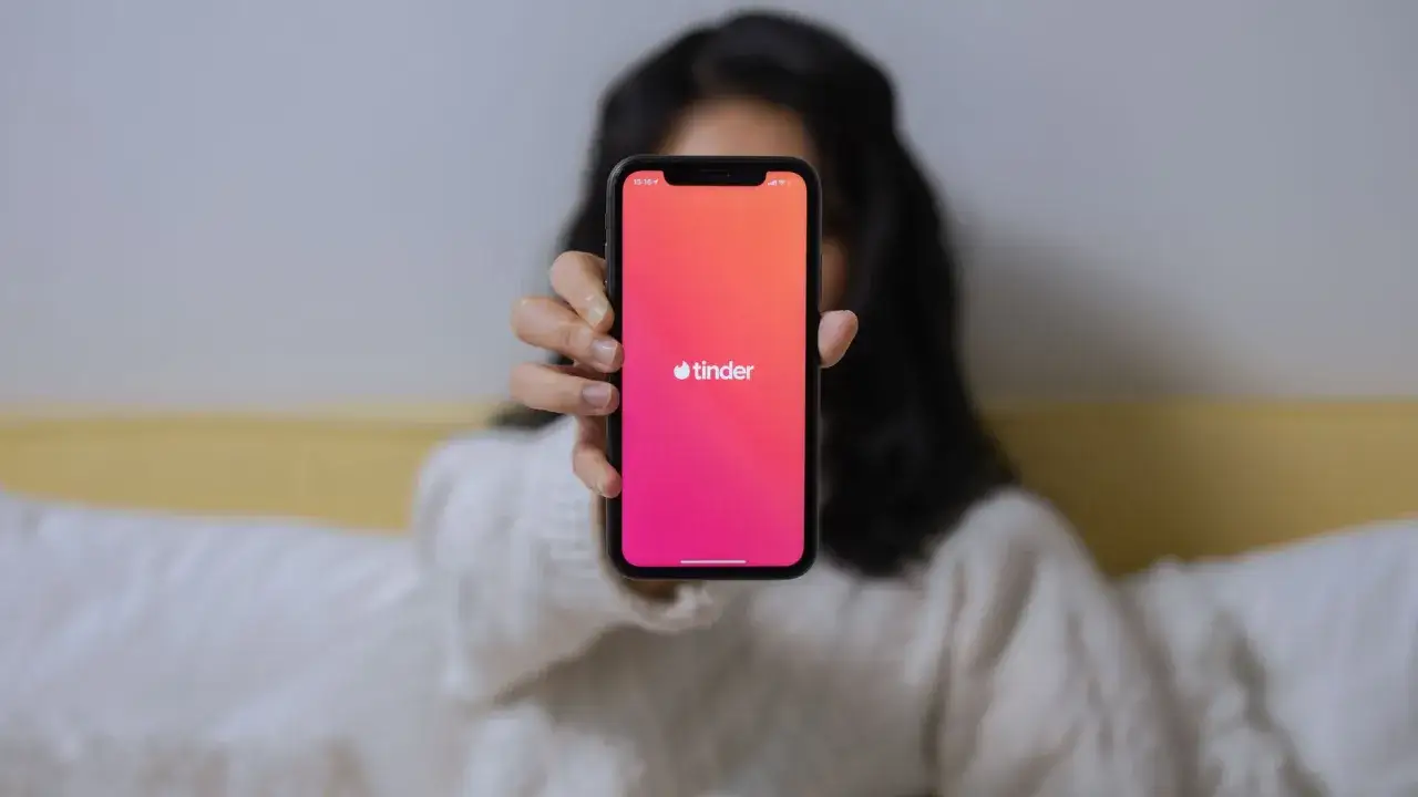 Osoba trzyma telefon z widocznym logo Tindera. Chcesz wiedzieć, jak sprawdzić, czy ktoś ma Tindera?