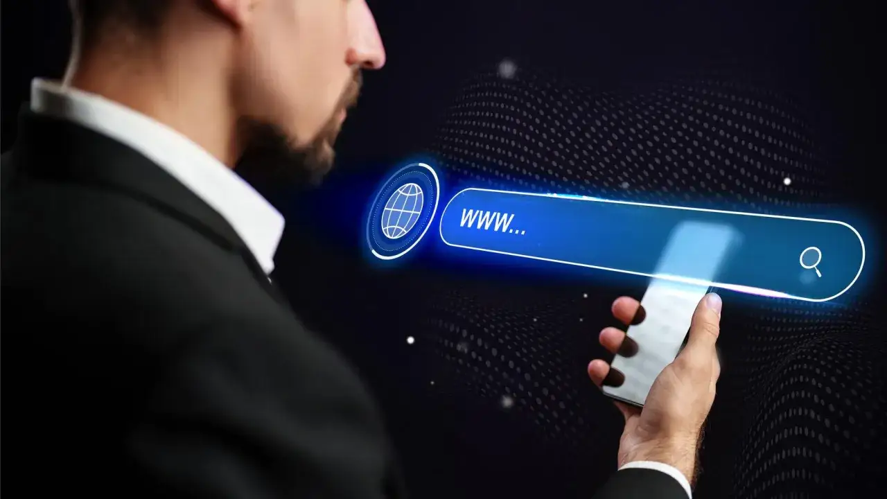 Mężczyzna w garniturze trzyma smartfon, na którym wyświetla się pasek wyszukiwania z ikoną globu i tekstem "www...".