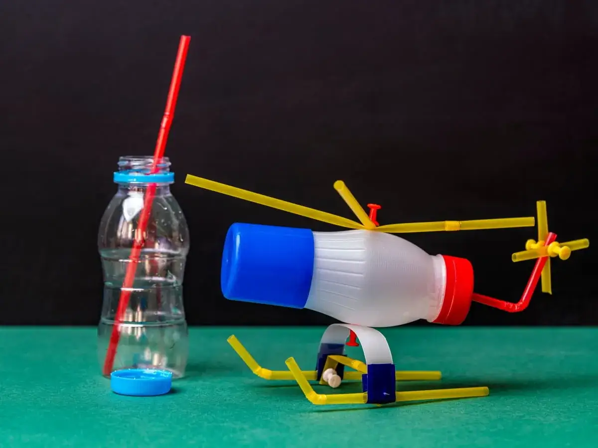 Helikopter z butelki i słomek obok butelki z czerwoną słomką.