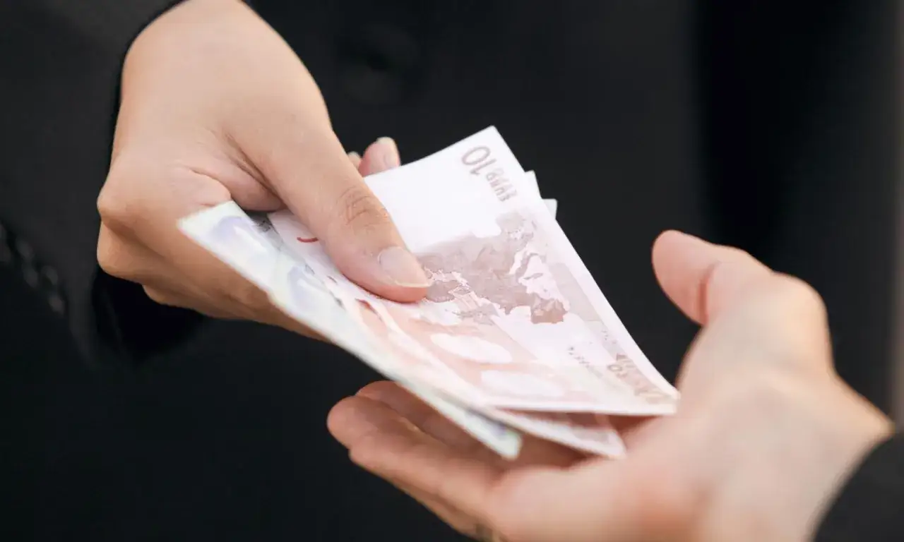 Dwie dłonie przekazują sobie banknoty euro. Zastanawiasz się, ile kosztuje windykacja należności?