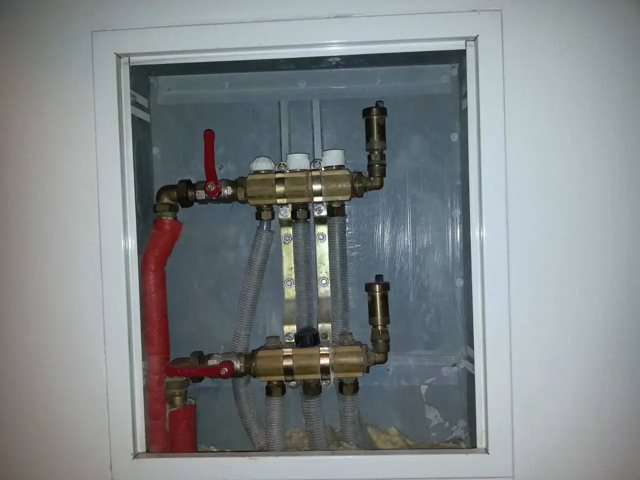 Widoczny zawór RTL na powrocie systemu ogrzewania podłogowego. Metalowa obudowa skrywa skomplikowaną instalację hydrauliczną.