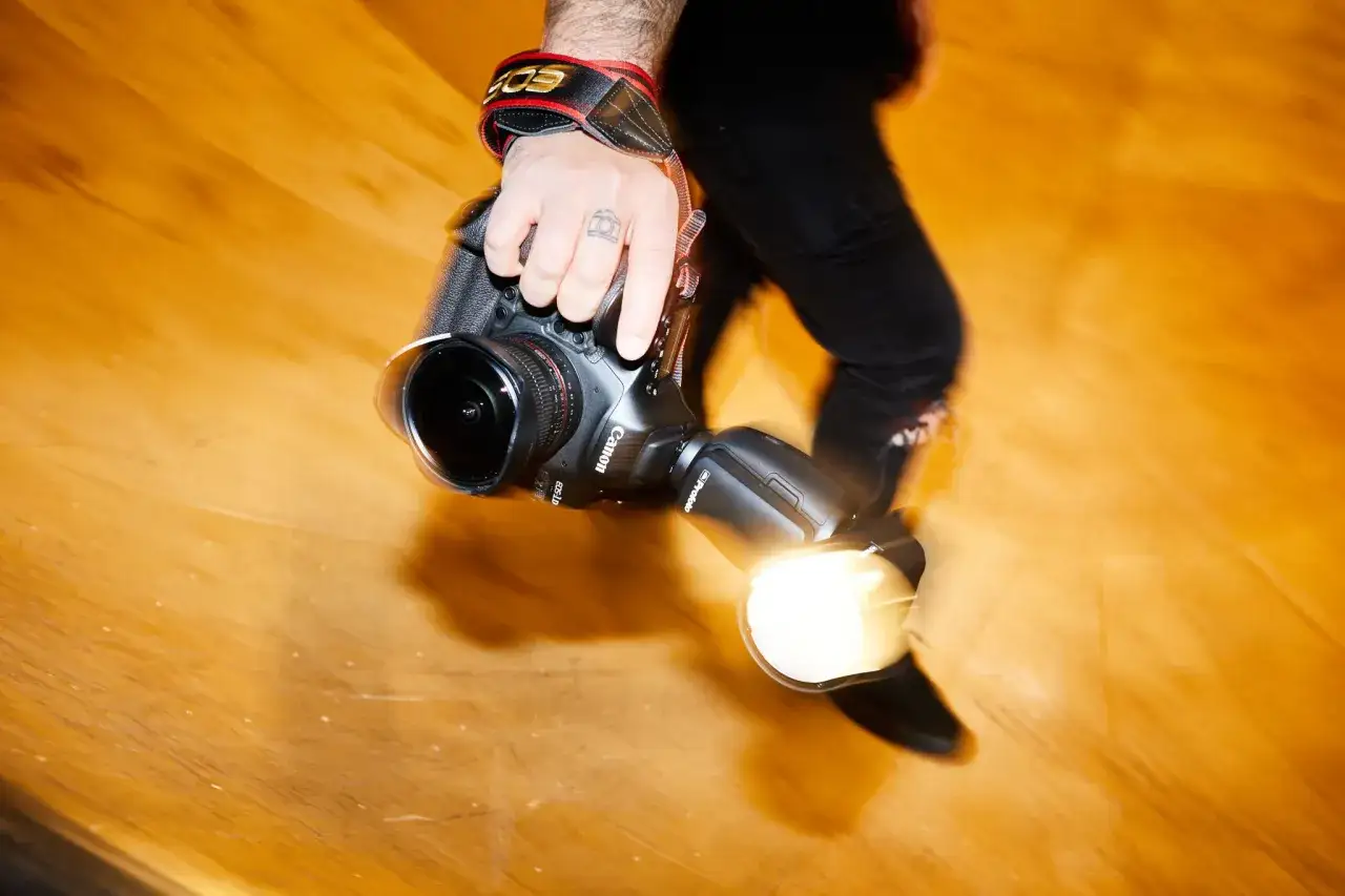 Dłoń fotografa trzyma aparat z lampą błyskową. Długi czas naświetlania tworzy efekt ruchu.