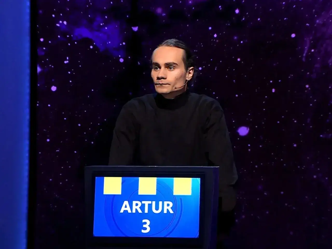 Artur, który wygrał jeden z dziesięciu, stoi na scenie w czarnym golfie.