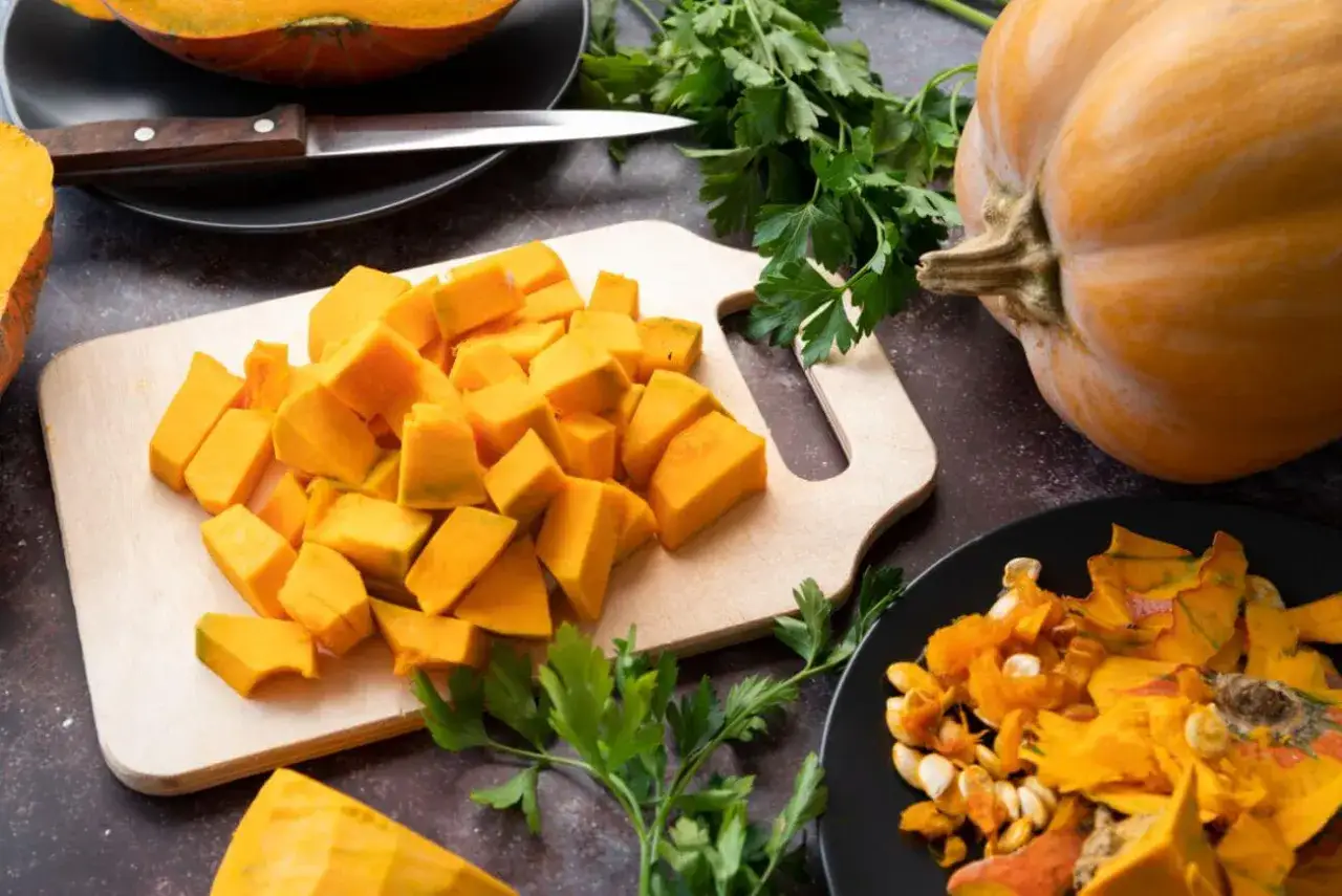 Pokrojona dynia na desce, obok cała dynia i resztki. Czy dynię można mrozić? Tak, pokrojona dynia świetnie nadaje się do mrożenia.